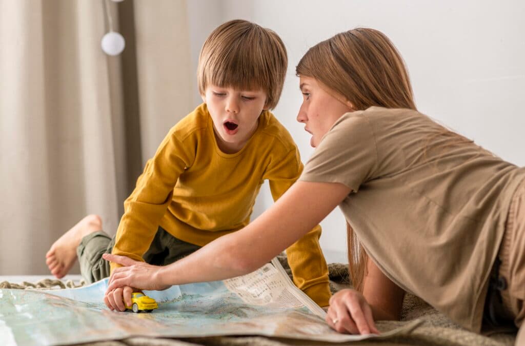 A mother and her young child playing together with a toy car on a large map spread across the floor